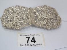 An art deco silver buckle pierced with cherubs toasting chalices amidst grape and vine,