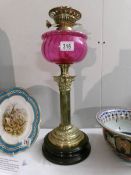 A brass oil lamp with Corinthian column and cranberry glass font (no shade or chimney)