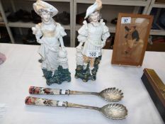 A pair of porcelain figures and a pair of salad servers