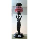 A Victorian oil lamp supported by a spelter figure and with a pink glass font,