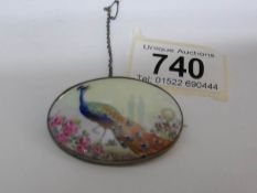 A hand painted oval brooch depicting a peacock among flowers by the Worcester painter Gresley
