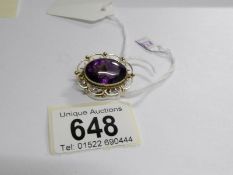 A gold brooch set with a large amethyst stone with filigree gold mount and safety chain