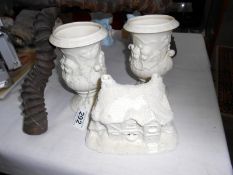 A pair of porcelain cherub urns and a cottage (one urn need base regluing)