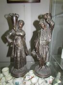 A pair of spelter figures carrying urns, both signed More?,
