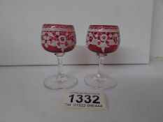 A pair of miniature cranberry glass goblets with enamel decoration