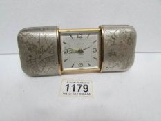 An Estyma sliding case travel clock with silver coloured case engraved with oriental fish