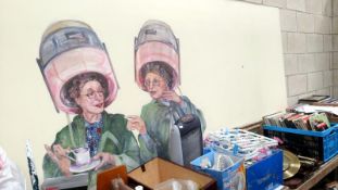 A large board with painting of 2 ladies under hair dryers