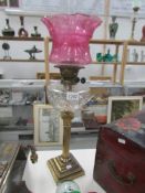 A brass Corinthian column oil lamp with cut glass font and acid etched cranberry glass shade
