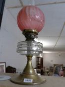 A Victorian oil lamp with glass font and etched cranberry glass shade