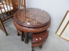 A heavily carved circular table with glass top and 4 smaller tables nesting underneath