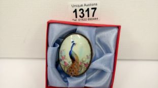 An oval enamel brooch depicting a peacock amongst flowers by the Royal Worcester painter C Gresley