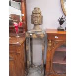 A carved wood Buddha head on a wooden stand