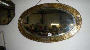 An oval bevel edged mirror in hammered brass effect frame