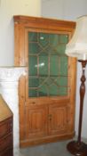 A pine corner cupboard with glazed door