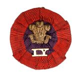 An Imperial Yeomanry slouch hat badge, brass POW’s feathers and “IY” on purple/scarlet rosette. GC