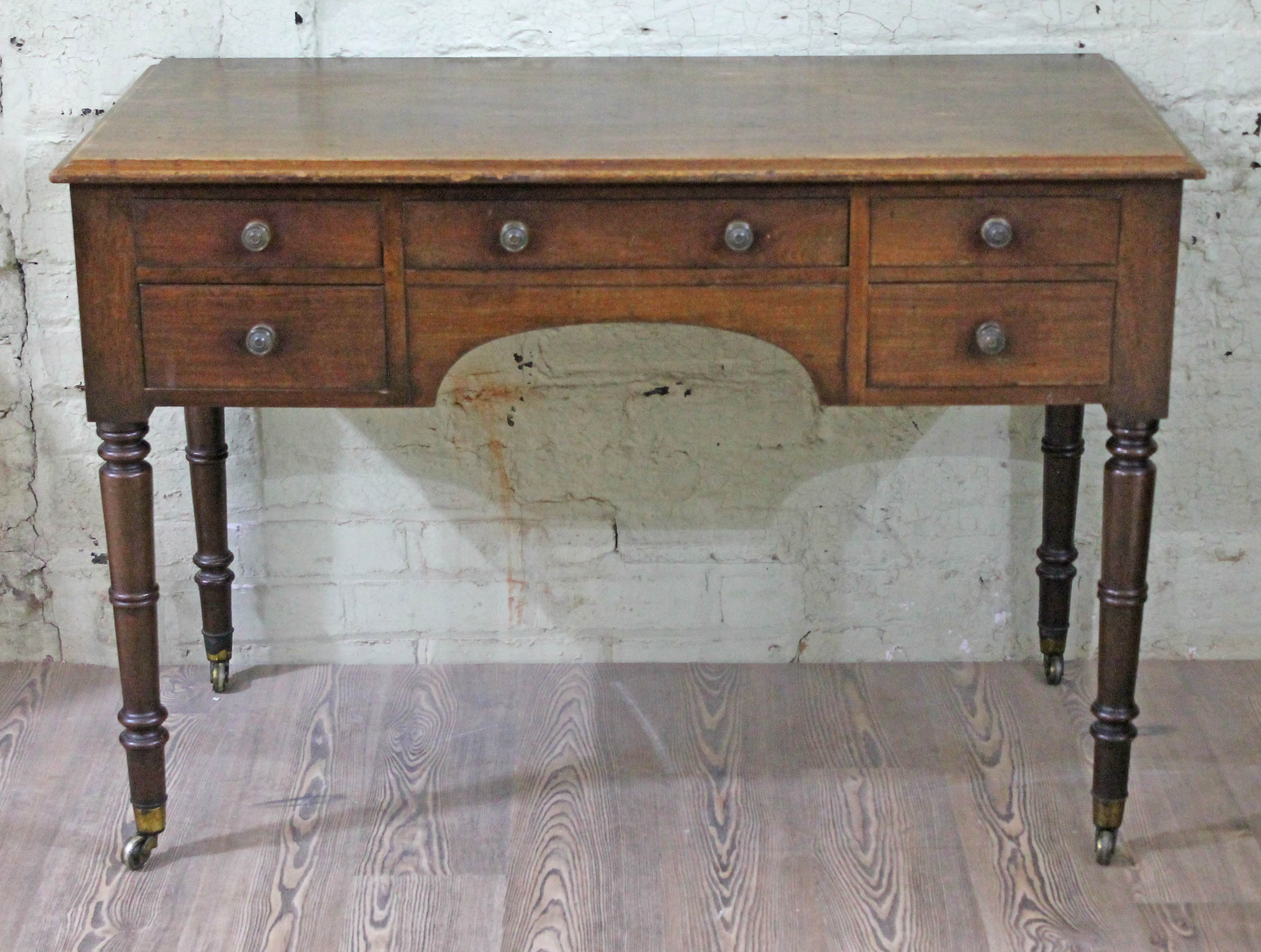 A Regency mahogany side table or desk with five drawers, turned legs with brass castors, width