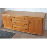 An Ercol light elm sideboard having three central drawers flanked by two cupboards and raised on