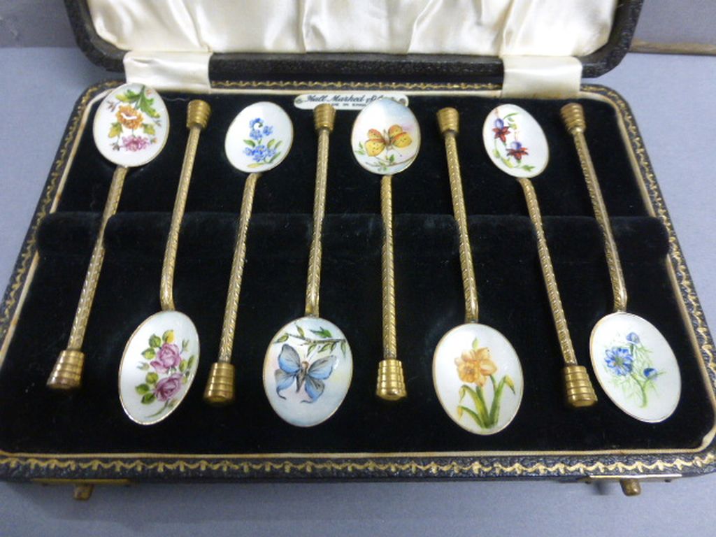 A cased set of early 20th century brass spoons, each enamel bowl painted flowers and plants, cased