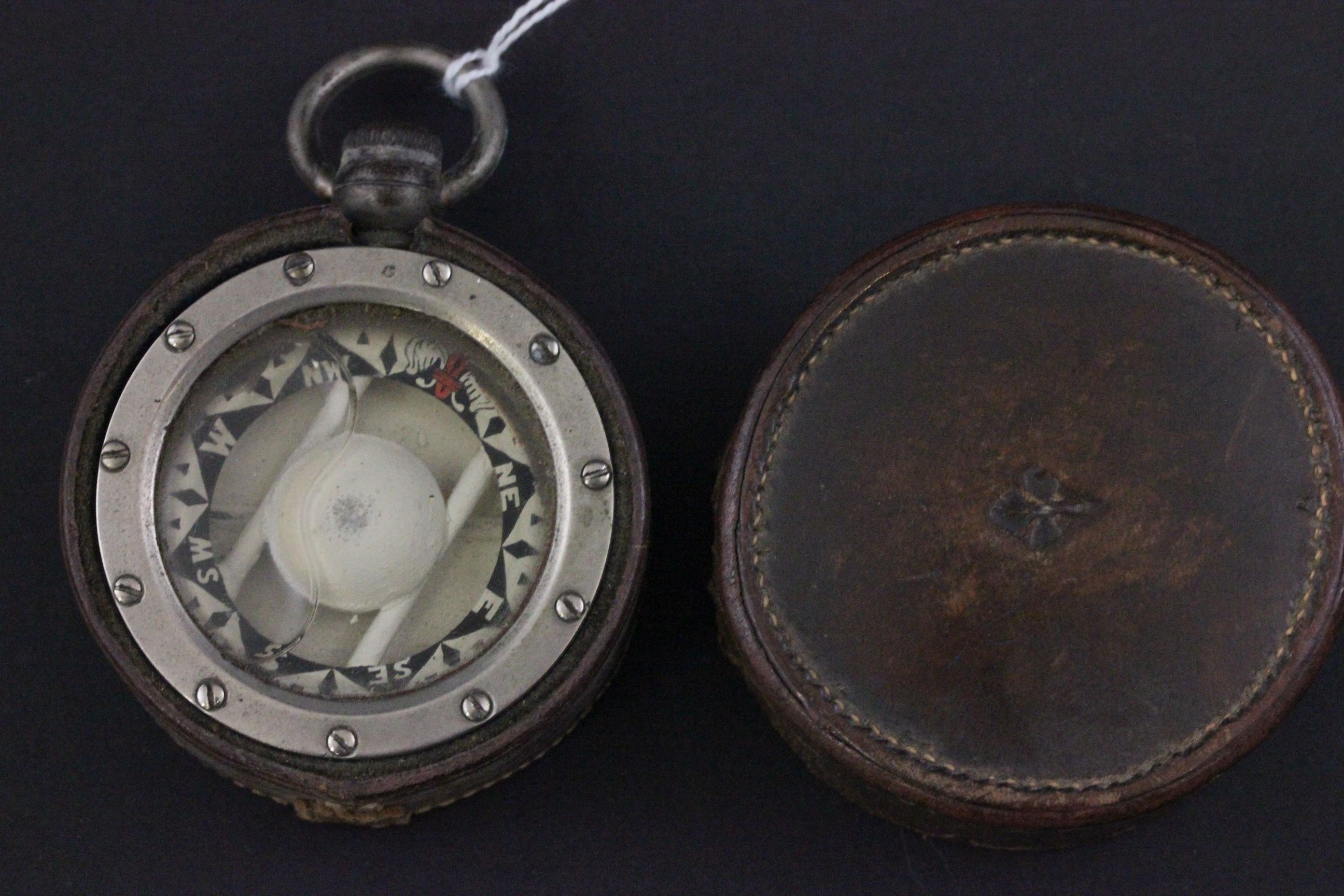 A vintage steel cased compass with leather case which is stamped with a Fleur de lis motif