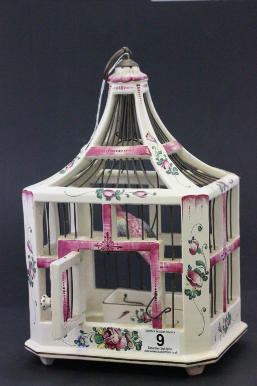 A interesting Faience bird cage with hand painted bird perched on a swing, with a detachable bird