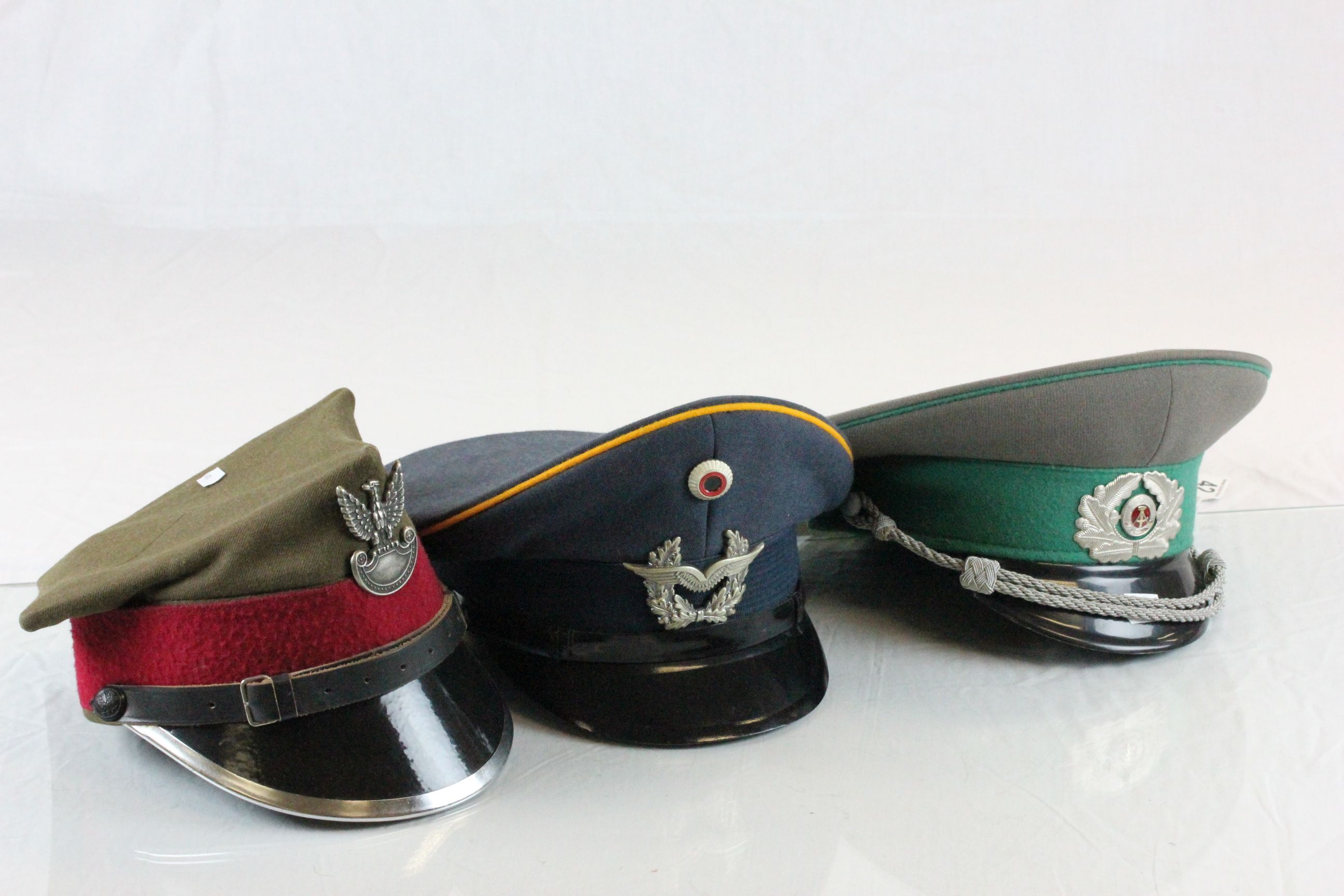 Three East German/ Polish military hats with badges