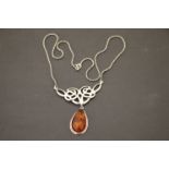 A silver necklace with large central amber style drop