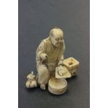 A meiji period carved ivory okimono of a seated man cooking.