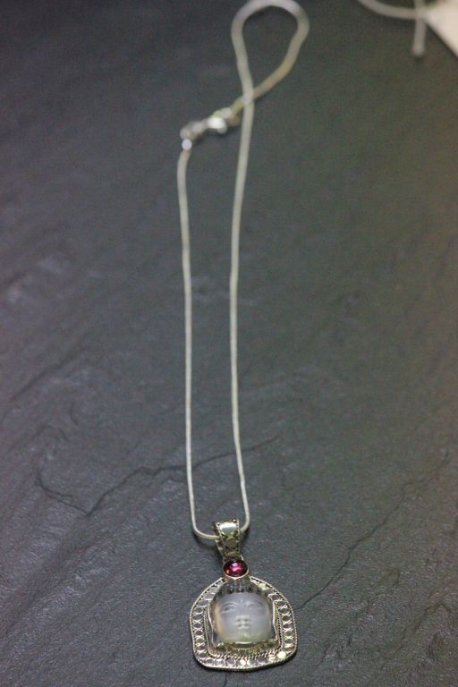 A silver rock crystal buddha pendant necklace with pink sapphire mount