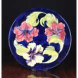 A Moorcroft Charger decorated with hibiscus on a dark blue ground, 12 ins (30 cms) in diameter.
