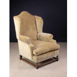 An Upholstered Hump-backed Wing Armchair covered in a tawny gold velvet and standing on short oak