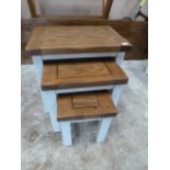 A set of three off white nest of tables with a rustic oak top