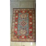 A small hand knotted woolen rug with a blue field - 115cm x 80cm - some wear to fringes but