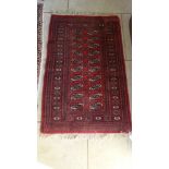 A small hand knotted woolen rug with a red field - 137cm x 80cm - some wear mainly to fringes