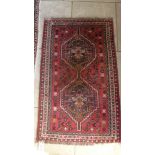 A small hand knotted woolen rug with a red field - 132cm x 79cm - some wear mainly to fringes