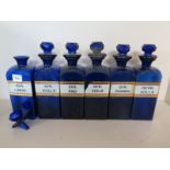 Six blue glass chemist bottles with stoppers - one stopper broken, one label chipped,
