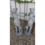 A pair of cast stone garden sculptures of whippets seated on an octagonal base - Height 80cm