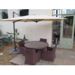A rattan style circular garden table with four armchairs and telescopic parasol with a granite
