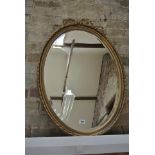 An oval gilt framed mirror with top decoration - 88cm x 60cm