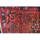 A hand knotted woolen rug with a red field - 2.00m x 1.