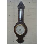 A 1930s carved oak barometer with a thermometer over a silvered dial,