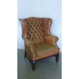 A modern tan leather covered button back armchair with mahogany legs