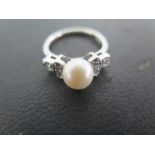 A 9ct white gold ring with 7mm cultured pearl flanked by six 2mm brilliant cut diamonds pave set