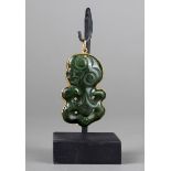 A hei-tiki pendant nephrite with a gilt metal mount, 4.8cm high, on a stand. (2)