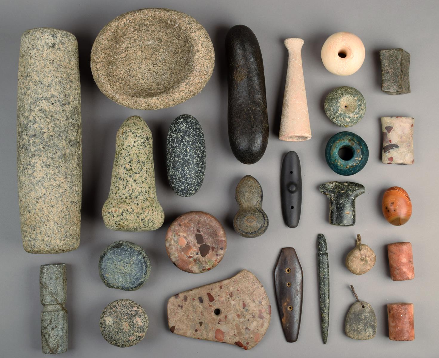 A collection of stone beads, implements and weights including an ovoid mortar and associated pestle,