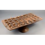 λA West African mancala board wood raised on a central column with thirty two wells, 58cm wide, with