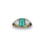 An emerald and diamond three stone ring, the emerald cut emerald is set with a trillion cut