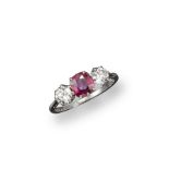 A ruby and diamond three stone ring, the cushion-shaped ruby is set between two old circular-cut