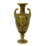 A tall Burmantofts Faience urn vase, footed form with pulled handles, moulded in relief with a