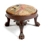 A George II mahogany circular stool, with a needlework seat worked with a parrot, on leaf carved