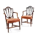 A pair of George III and later shield back open armchairs, each carved with foliage, husks and